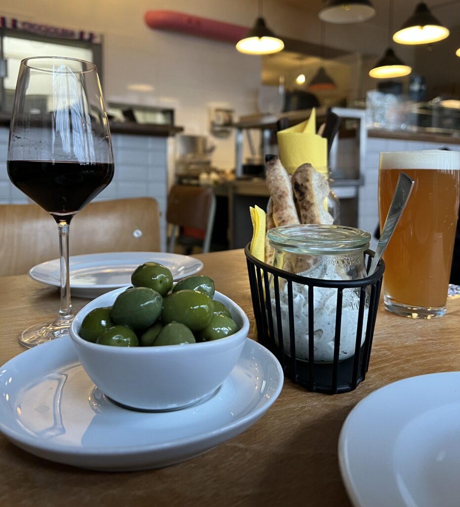 A bowl of Italian green olives, a glass of red wine and a pint of fresh craft beer on a table of an Italian pizza restaurant in Berlin. 