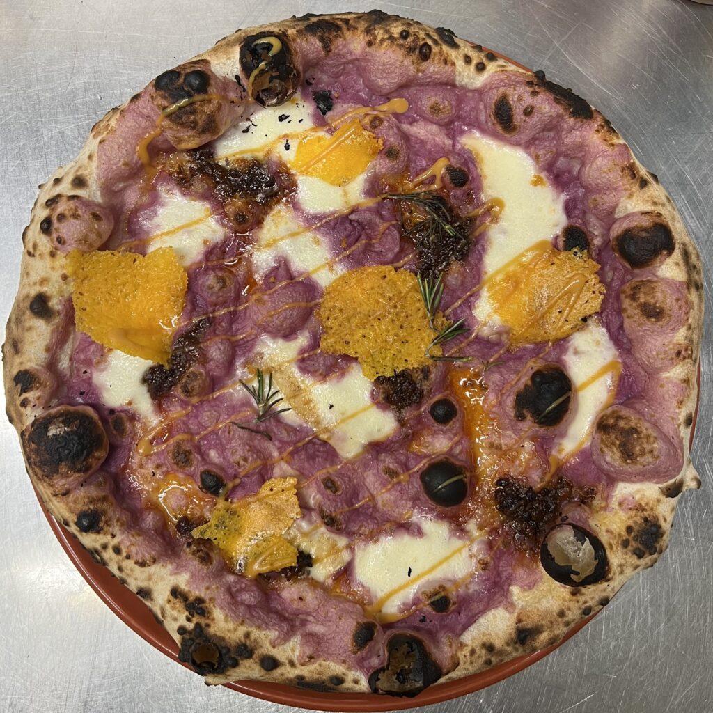 Authentic Neapolitan pizza with violet potatoes, smoked mozzarella, cheddar cheese, bacon jam, and mustard at a Berlin pizzeria.
